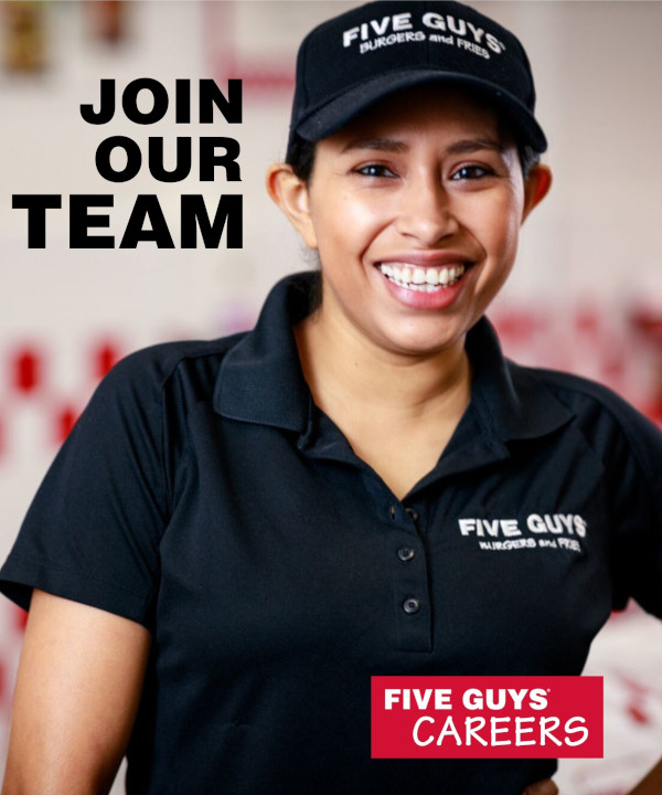 A photograph of an Five guys female manager in black shirt and black hat smiling at the camera.